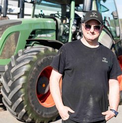 Milchkuhhalter Basti Bützler am Morgen des 1. Grasschnitts vor einem Traktor.