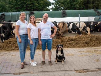 Die Geschwister Stefanie van Look, Katharina Verhaelen und Rainer Mott stehen mit dem Hofhund vor dem Futtertisch
